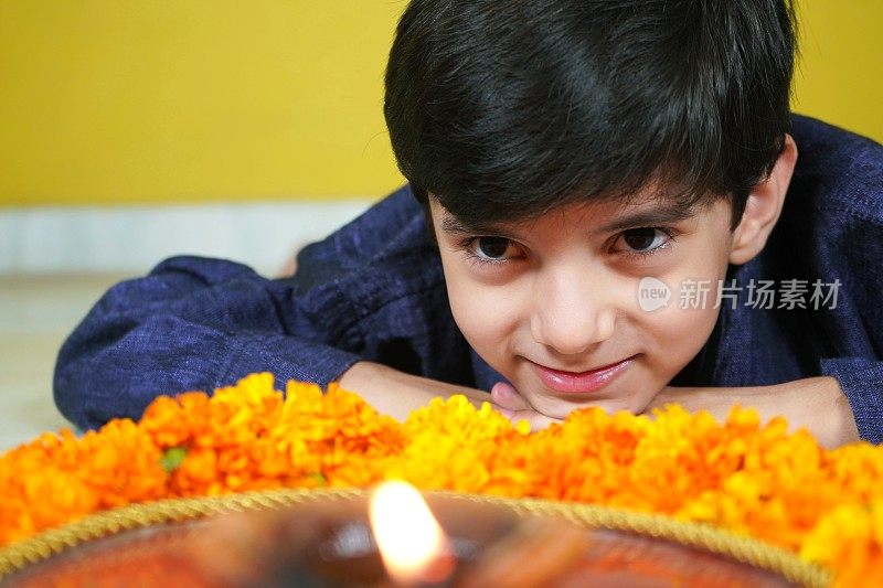 一个快乐微笑的印度亚洲男孩看着一个Pooja或祈祷塔利与火焰，Jyot, Diya, Deepak火焰和金盏花
